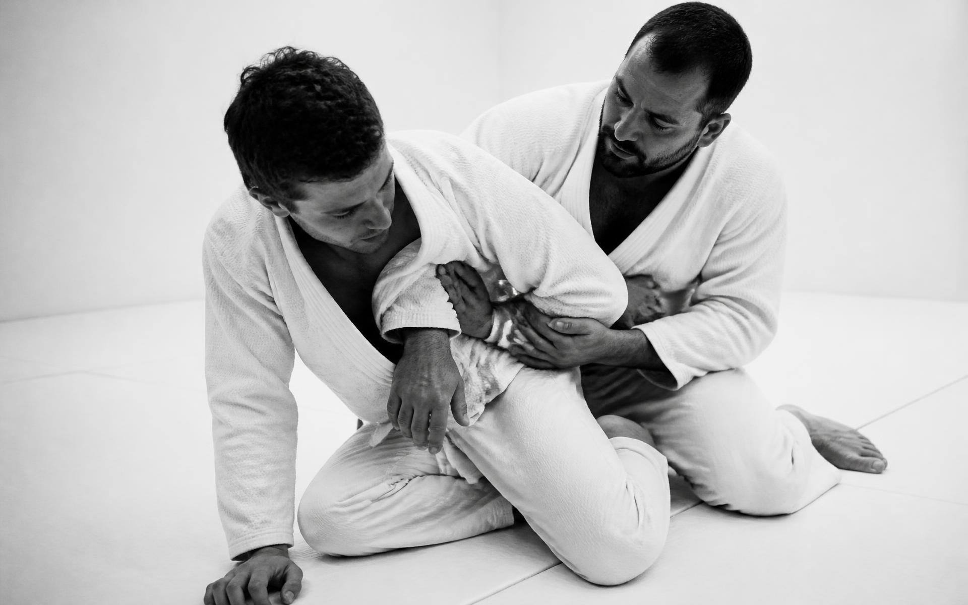 Instrutor ensinando técnica de jiu-jitsu a um aluno iniciante no tatame
